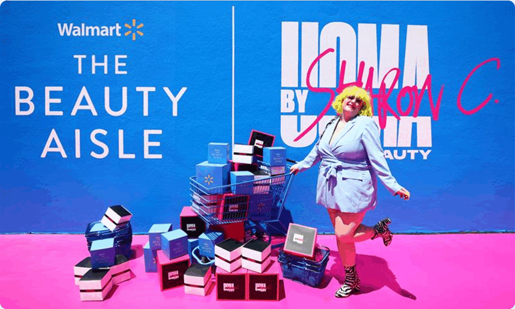 A woman in a stylish blue suit standing with UOMA cosmetics at the Walmart Beauty Aisle event. Standing on a pink carpet.